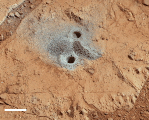 A Drill hole in the Yellowknife Bay, made by the Mars Curiosity rover. The drill hole is 1.6 cm in diameter, and the white scale bar at the bottom right of this picture is 2 cm in length (Photo Credit: University of Leicester).